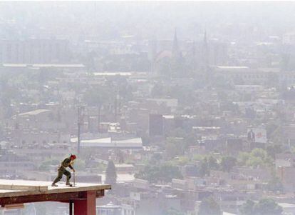 Un trabajador de la construcción en la parte superior de un edificio. Al fondo la nube contaminante