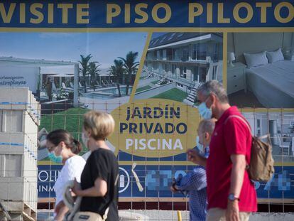 Varias personas caminan ante un cartel de viviendas en venta en A Mariña (Lugo), el pasado 26 de julio.