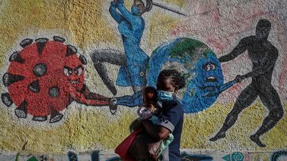 Una mujer con un bebé en brazos pasa delante de un mural que simboliza la lucha contra el coronavirus en una calle de Kericho, Kenia.