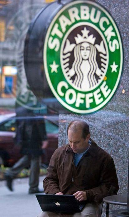 Un hombre con su portátil en la terraza de una cafetería de la cadena Starbucks.