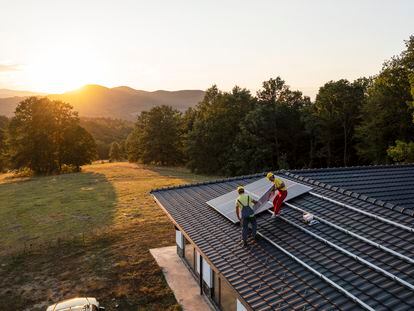 Operarios colocan una placa fotovoltaica en el tejado de una vivienda.