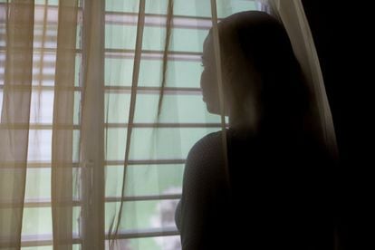 A teenager looks out the window without letting her face be seen to protect her identity.