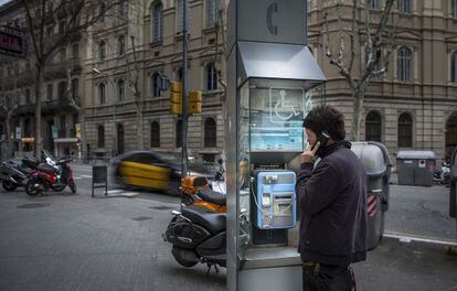 Un joven habla por teléfono desde una cabina en una calle de Barcelona y a cuyo mantenimiento se dedica la empresa Imesapi.