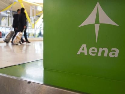 Dos viajeros pasan ante un cartel de Aena en el aeropuerto de Madrid-Barajas.