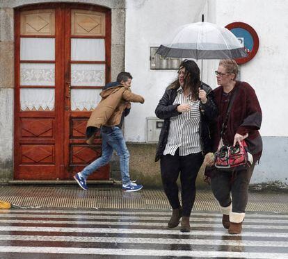 Vecinos de Melide (A Coruña) se protegen de la lluvia y el viento.