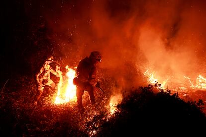 Dos bomberos trabajan esta pasada noche en la extinción de un incendio en Piedrafita, en Asturias.