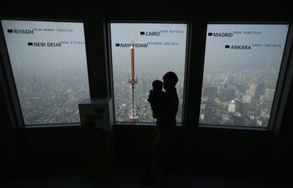 Un hombre con su bebé en brazos se asoma al mirador de la 'Torre N de Seúl'. El perfil de la ciudad está cubierto por una intensa capa de polución.
