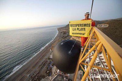 Un activista sobre la bola de demolición simbólica que han instalado hoy en una de las grúas que rodean el hotel de El Algarrobico.