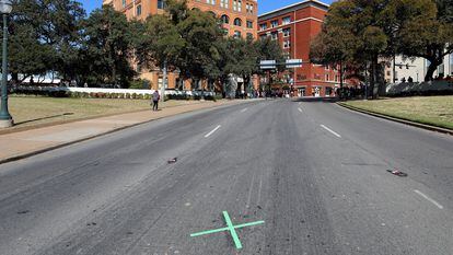 La X en la calzada de Dealey Plaza (Dallas) que marca el lugar donde Kennedy recibió el tercer impacto de bala. Al fondo, The Sixth Floor Museum, donde en 1963 se encontraba el depósito de libros escolares desde el que Oswald disparó al presidente.