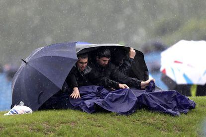 Tres aficionados tratan de cubrise de la lluvia en el circuito de Silverstone