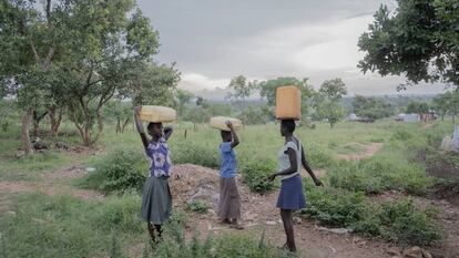 Tres mujeres llevan bidones llenos de agua desde un pozo hasta sus hogares en el campo de refugiados Rhino Camp, en Uganda.