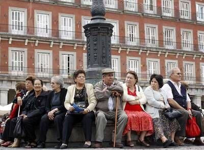 Un grupo de personas mayores contempla la plaza Mayor desde un banco.