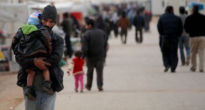 Un hombre sirio carga a su hijo en un campo de refugiados en la frontera de Jordania cerca de Siria.