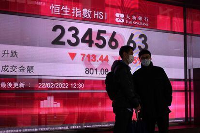 People talk as they stand beside an electronic board showing numbers of the Hang Seng index in Hong Kong on February 22, 2022. (Photo by Peter PARKS / AFP)
