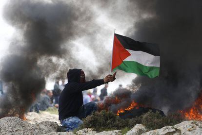 Un manifestante sostiene una bandera palestina mientras el humo emerge de los neumáticos quemados durante enfrentamientos con las fuerzas de seguridad israelíes, cerca de la ciudad cisjordana de Ramallah.