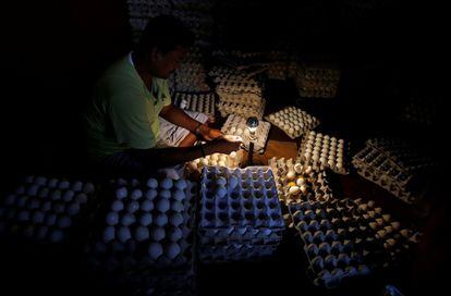 Un trabajador revisa los huevos con una bombilla dentro de una tienda al por mayor en un mercado en Calcuta (India).