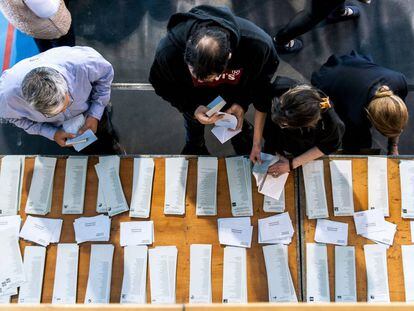 Electores en mesa de papeletas y sobres en un colegio electoral.