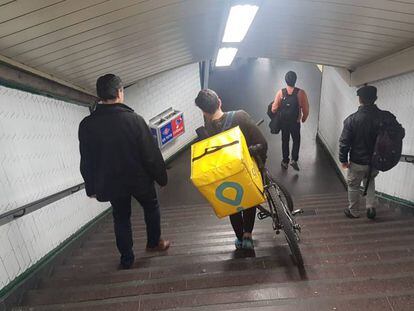 Un joven baja las escaleras de una estación de metro de Madrid con una bicicleta de reparto de pedidos a domicilio.