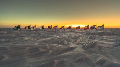 Banderas de los primeros países signatarios del Tratado Antártico tras el marcador del Polo Sur ceremonial, a unos metros del geográfico.