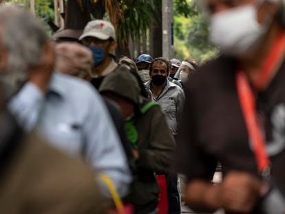 Varios hombres esperan en una fila a recibir alimentos de forma gratuita en la Ciudad de México.