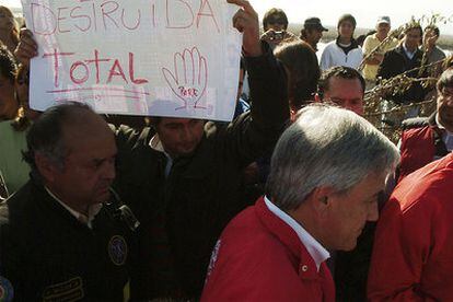 Sebastián Piñera visita el puerto de Talcahuano, destrozado por el <i>tsunami</i>. A su paso, un vecino muestra un cartel con el lema <i>Destrucción total</i>.