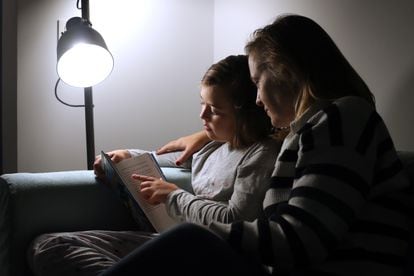 An 11-year-old girl reads a book with her mother at home. 