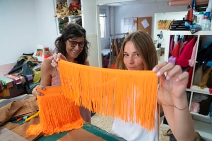 Ángela muestra a cámara una tira con los característicos flecos de seda de Gloriaca, un guiño a su identidad española. De fondo, Gloria, la diseñadora, sostiene el bolso.