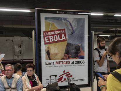 Unos turistas esperan un tren en la estación de Barcelona Sants junto a un cartel de lucha contra el ébola en 2014.