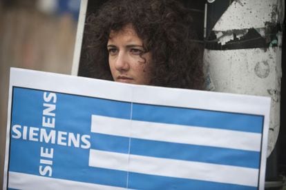 Una activista griega protesta en Berlín con una bandera que incluye el nombre de una empresa alemana.