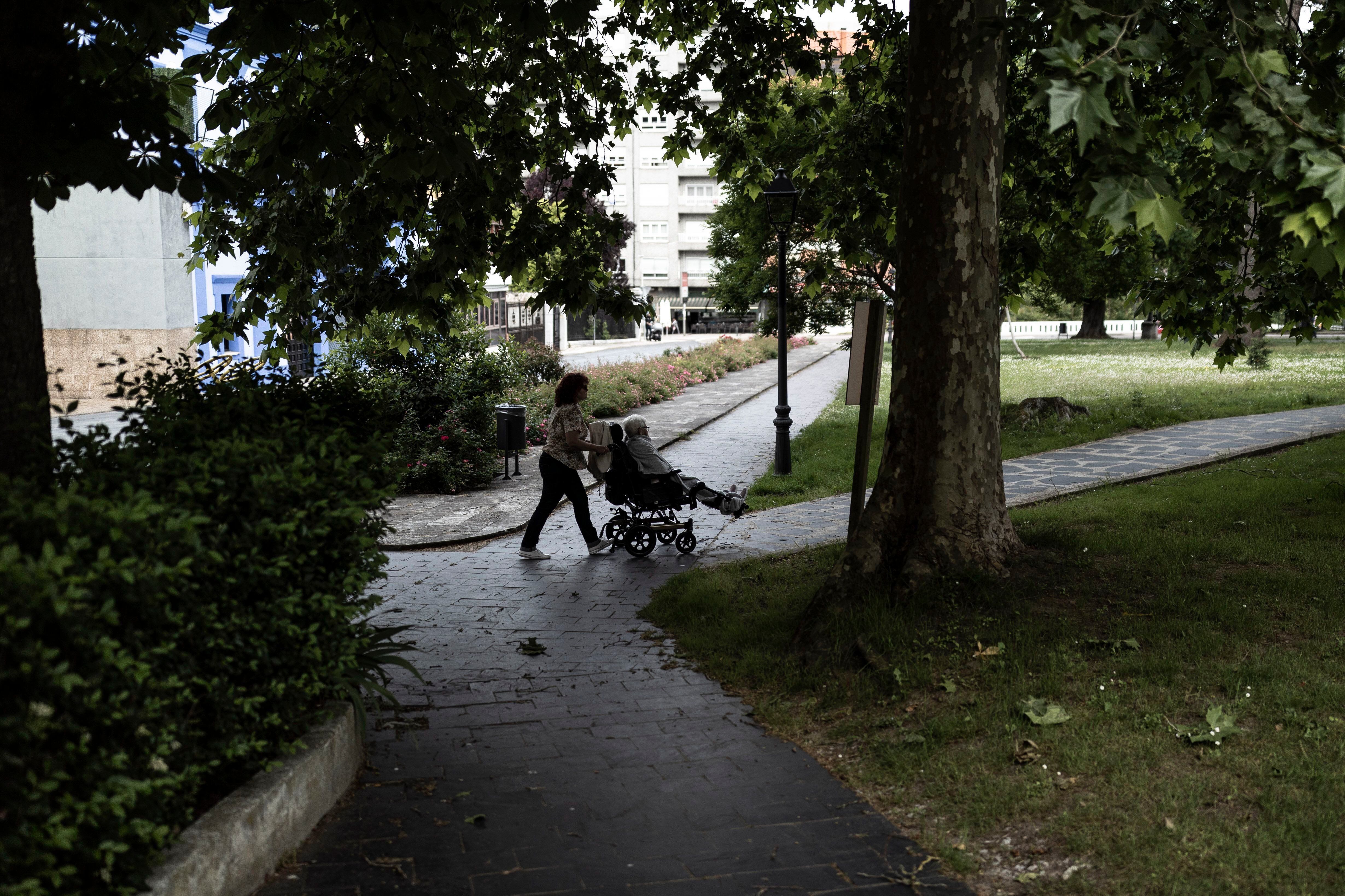 Una mujer empuja a una anciana en silla de ruedas en un parque en Grado.