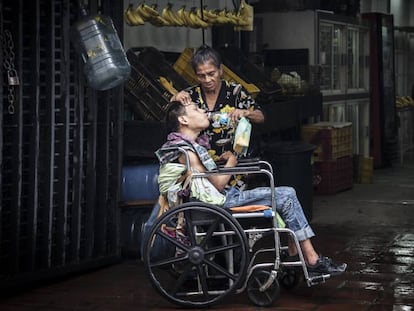 Una madre da de beber agua a su hijo postrado en una silla de ruedas en Caracas.