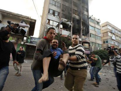 Dos hombres transportan a un herido despu&eacute;s de que la Aviaci&oacute;n israel&iacute; alcanzara el edificio que alberga los centros de prensa en Gaza.