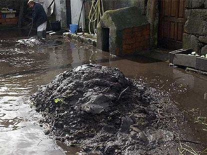 Una vecina de Pazos (A Coruña) limpia el lodo acumulado en la entrada de su casa debido a las lluvias.