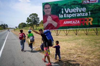 El venezolano Aliender Zarraga, un migrante que pone rumbo a Colombia con su familia, pasa delante de un cartel del candidato chavista Jorge Arreaza en Barinas.