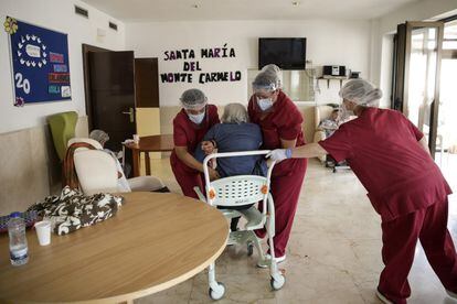 Tres trabajadoras asisten a una mujer mayor en la residencia Monte Carmelo.