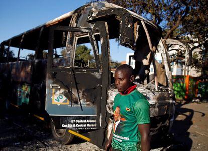 Un partidario del gobernante ZANU-PF pasa junto a un vehículo quemado en las oficinas del partido un día después de los enfrentamientos entre las fuerzas de seguridad y los manifestantes de la oposición en Harare