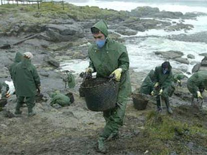 Varios voluntarios recogen restos de fuel en una zona de la costa de la localidad coruñesa de Muxía.