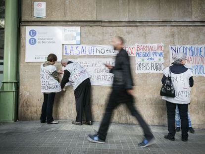 Membres de Tancada Clínic enganxen cartells contra la privatització a la façana del centre públic.
