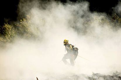 Un bombero se abre paso entre el humo de un fuego apagado. 
