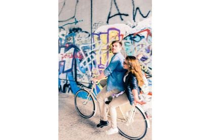 Una pareja pasa en bici ante un grafiti en Berlín.