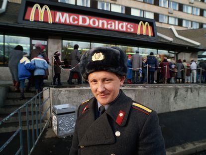 Un policía soviético sonríe a la cámara mientras, al fondo, se organiza una cola de horas para probar una hamburguesa en el primer día que abrió McDonalds en Moscú, el 31 de enero de 1990.