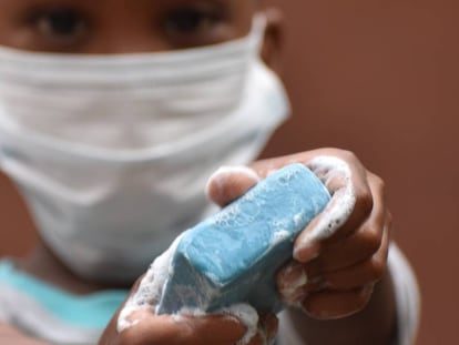 Un niño, con su mascarilla, sujeta un jabón para lavar sus manos.