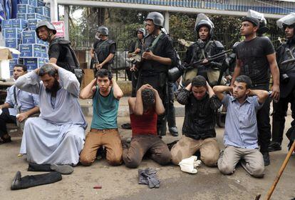 Varios miembros de las fuerzas de seguridad egipcias vigilan a un grupo de manifestantes arrestados durante el asalto a uno de los dos asentamientos de los simpatizantes del depuesto presidente Mohamed Mursi en la plaza del Nahda, cerca de la Universidad de El Cairo.