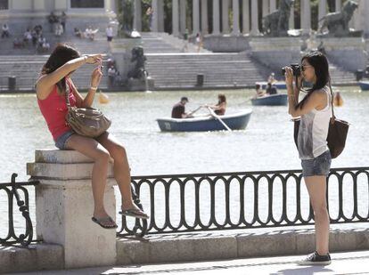 Dos turistas se fotograf&iacute;an en el parque del Retiro de Madrid mientras otros pasean en barca.