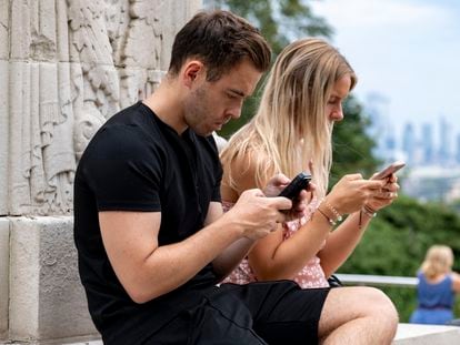 Dos personas utilizan el móvil en un espacio público.
