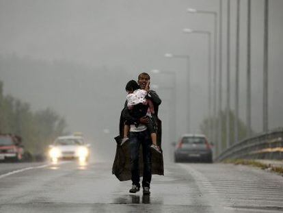 Un refugiado grita a sus compañeros que le esperen, mientras camina con su hija en brazos por una carretera griega hacia Macedonia.