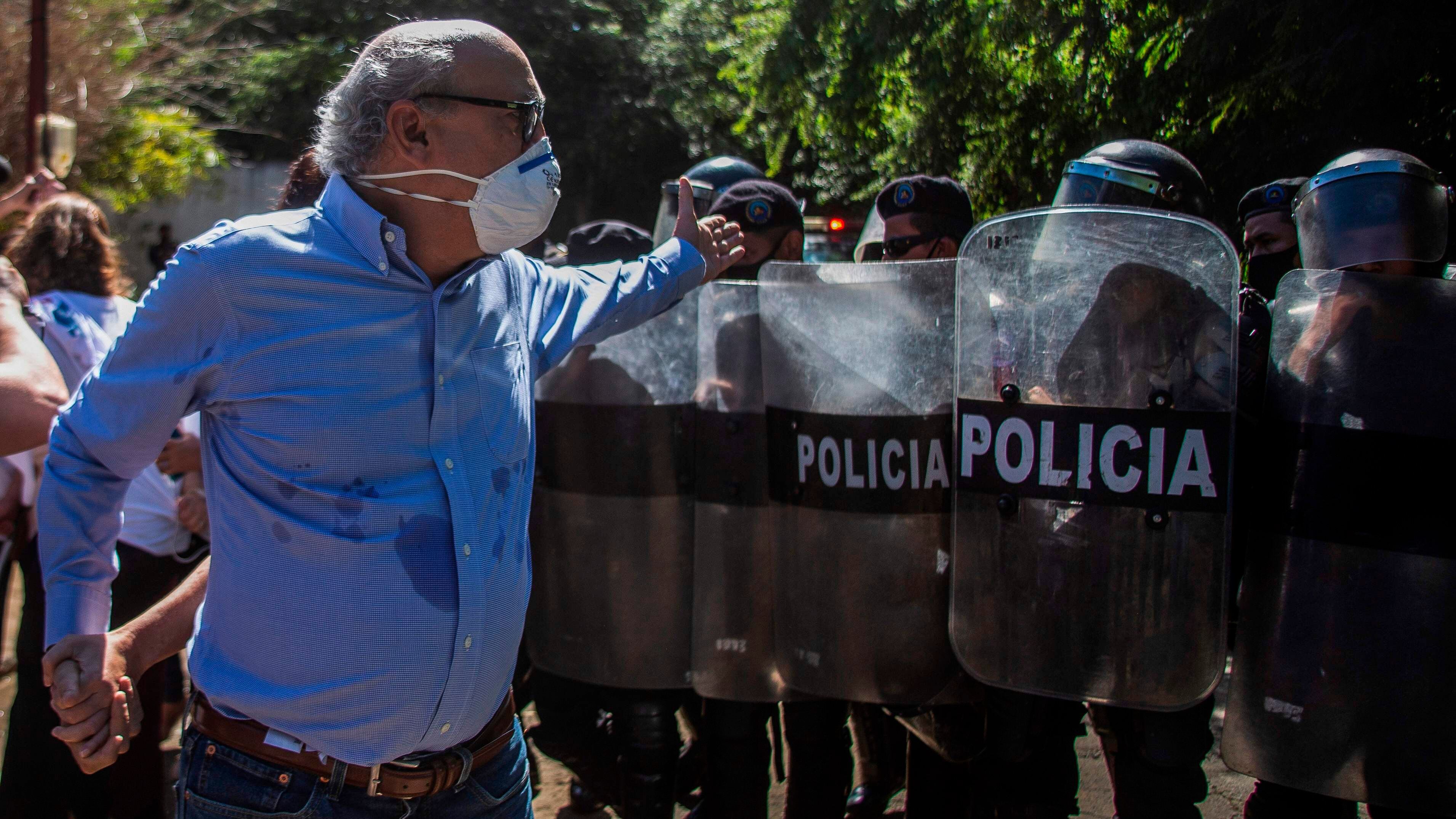 El periodista Carlos Fernando Chamorro en diciembre de 2020 frente a oficiales antidisturbios que custodian las instalaciones de la revista Confidencial, confiscadas por el régimen de Daniel Ortega.