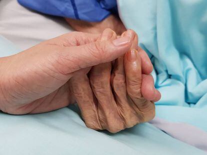 Una mujer coge la mano de una anciana en un hospital.