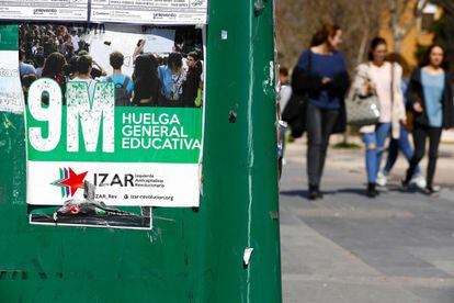 Tres estudiantes pasan junto a un cartel de la huelga general educativa, en la Universidad Complutense de Madrid.