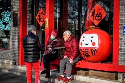 Varias personas mayores conversan en el exterior de un restaurante en una calle de Pekín. 